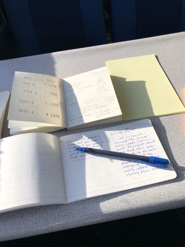 Image shows some notebooks on a train table with a blue pen resting over the top.
